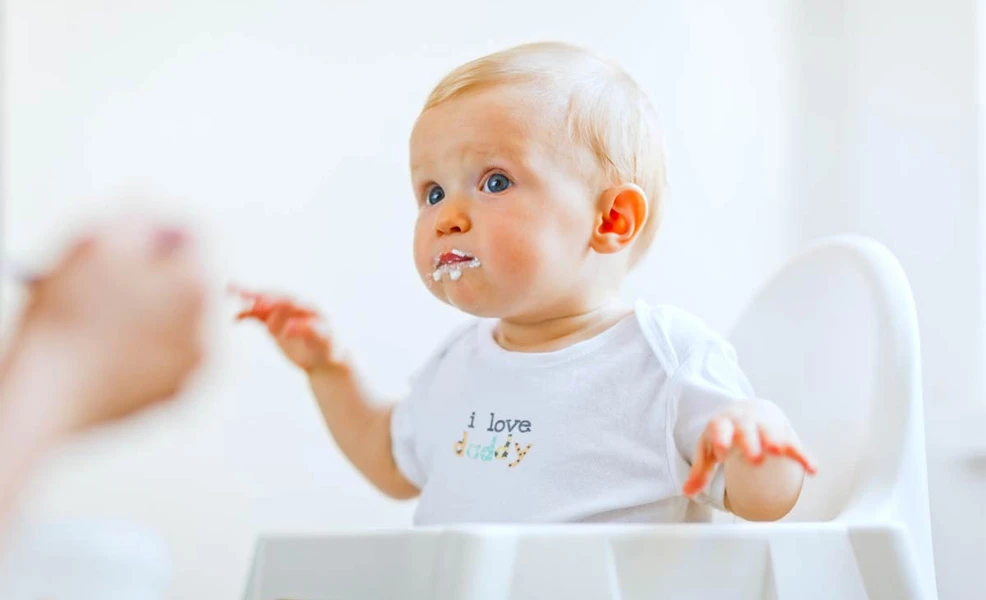 a baby sitting in a high chair being spoon-fed baby cereal