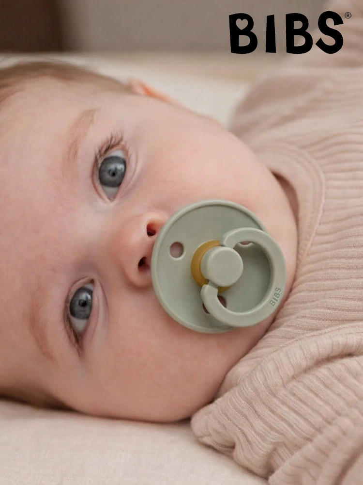 a baby laying down with a BIBS pacifier in its mouth