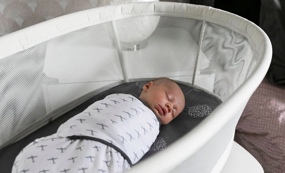 a swaddled baby sleeping in a halo bassinet