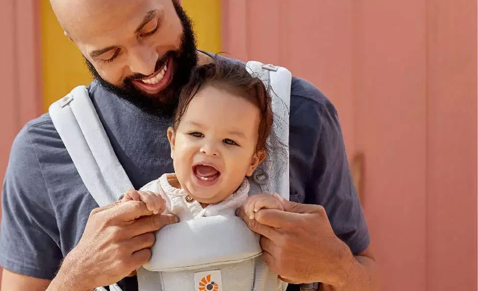 father wearing an ergobaby baby carrier with smiling baby