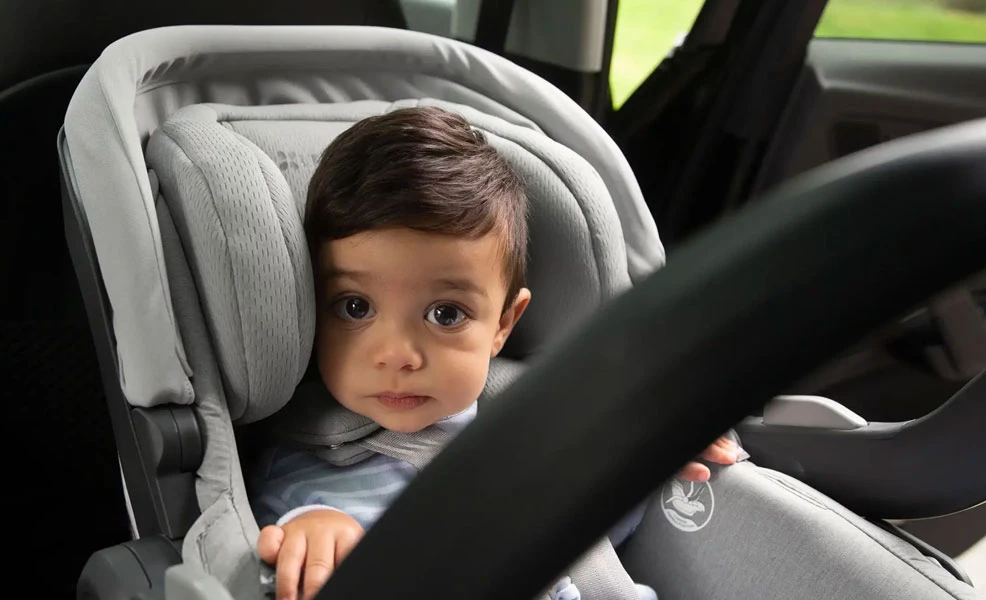 a toddler boy peeking out from the uppababy mesa infant car seat installed in a vehicle
