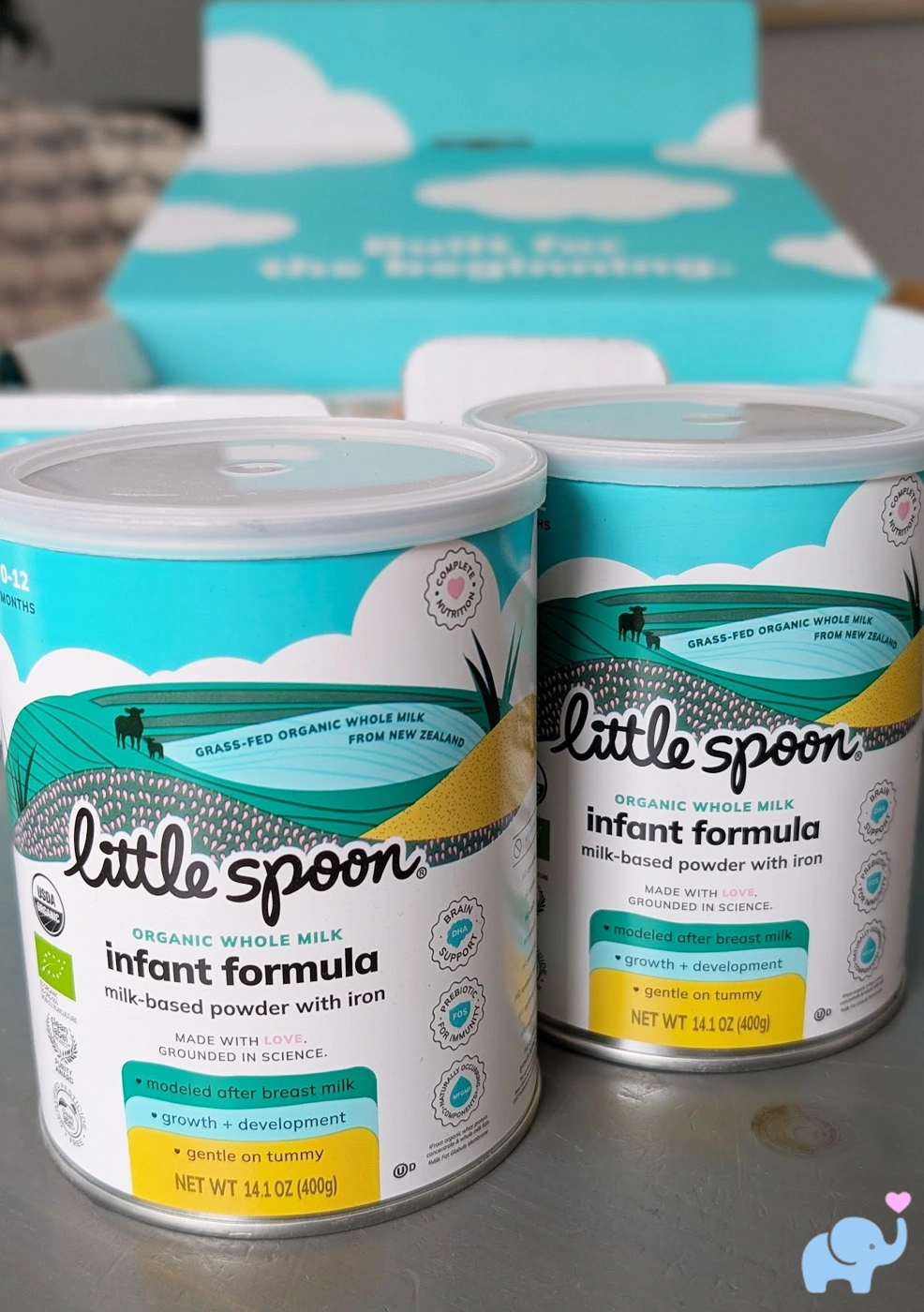 two tins of Little Spoon Organic Infant Formula sitting on a table with the opened box in the background