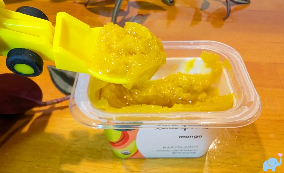 Little Spoon mango baby food with spoon showing thick textured puree