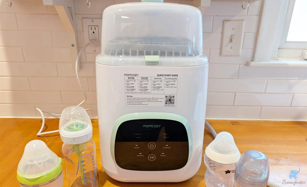 momcozy bottle washer on kitchen counter next to assorted baby bottles
