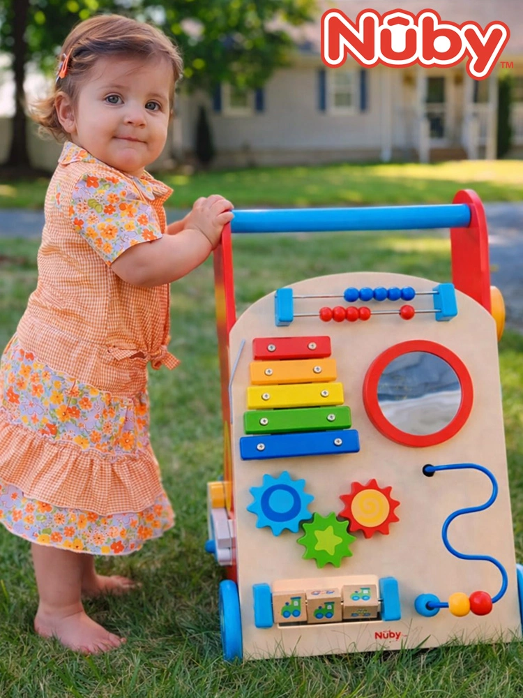 a baby girl standing next to the nuby wooden baby walker in the park