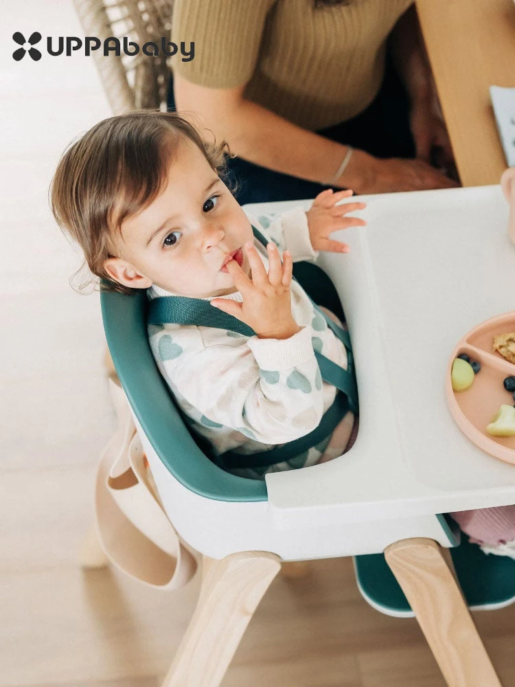 a toddler sitting in the uppababy ciro high chair and eating food